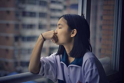 teenage girl thinking beside window